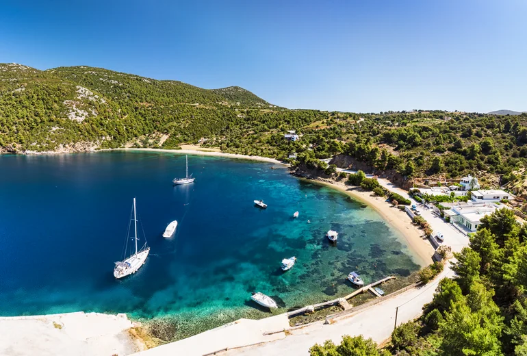 Acropolis on a hill above a Greek village with sailboats anchored in the bay below